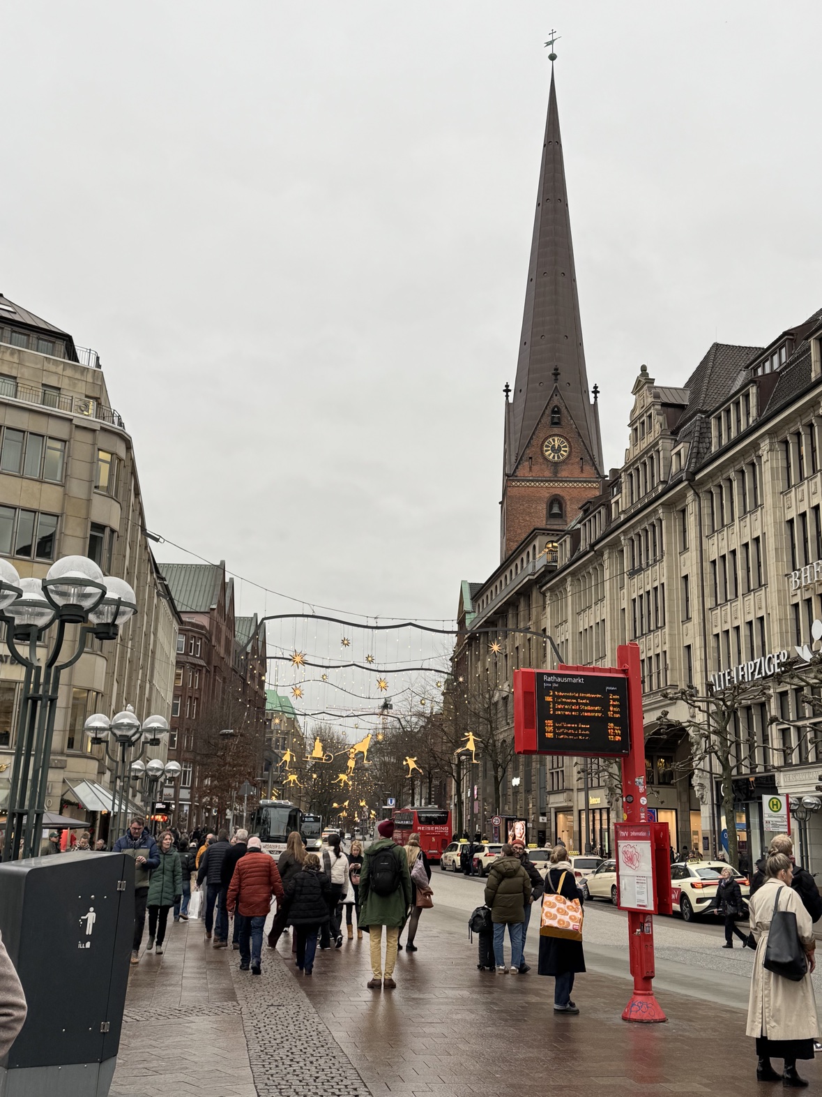 A Hamburg shopping street under golden Christmas lights, with the St. Petri church spire beyond