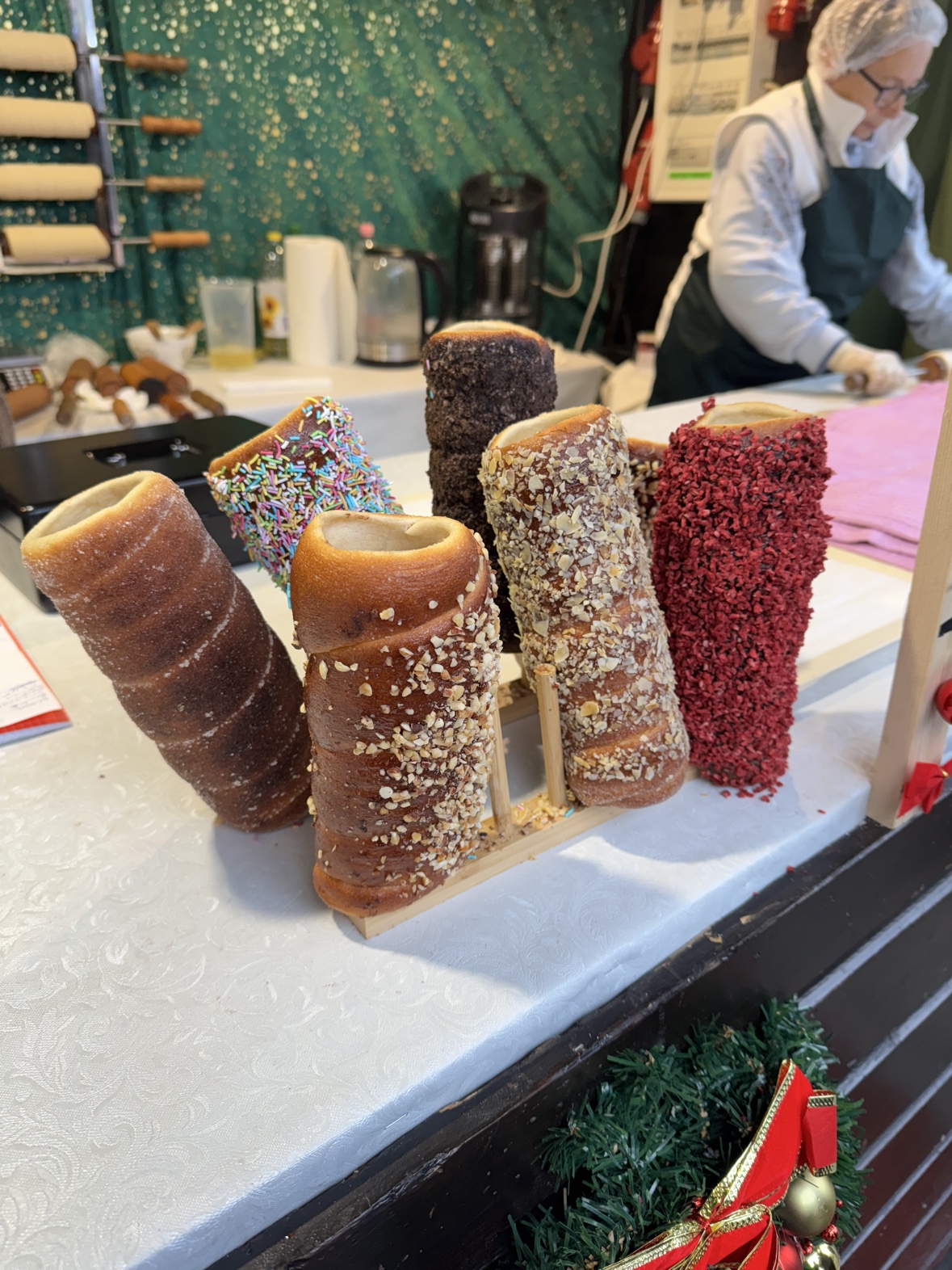Chimney cakes in assorted coatings — sugar, chopped nuts, chocolate, and sprinkles — on a stall at the Mannheim Christmas market