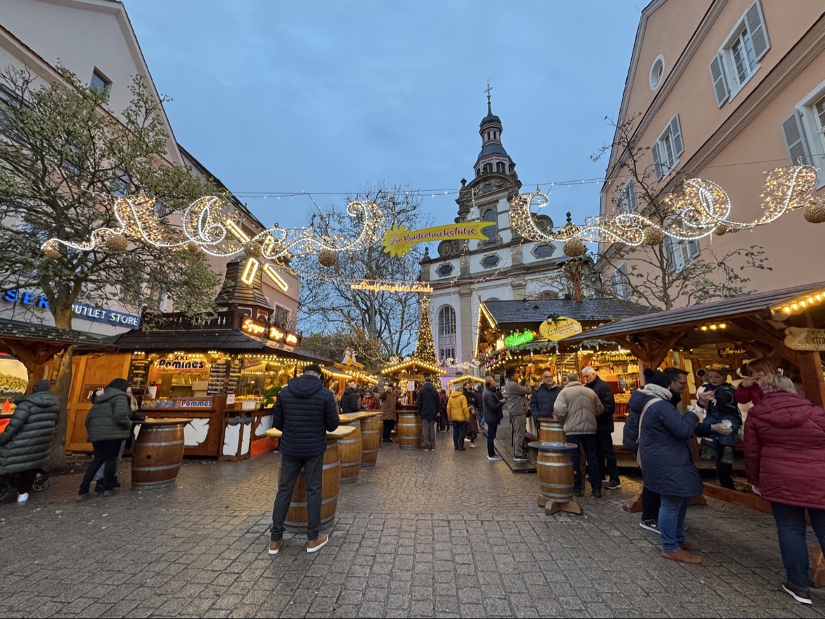 The Christmas market in Speyer, Germany, at dusk, with stalls and barrel tables under a church tower