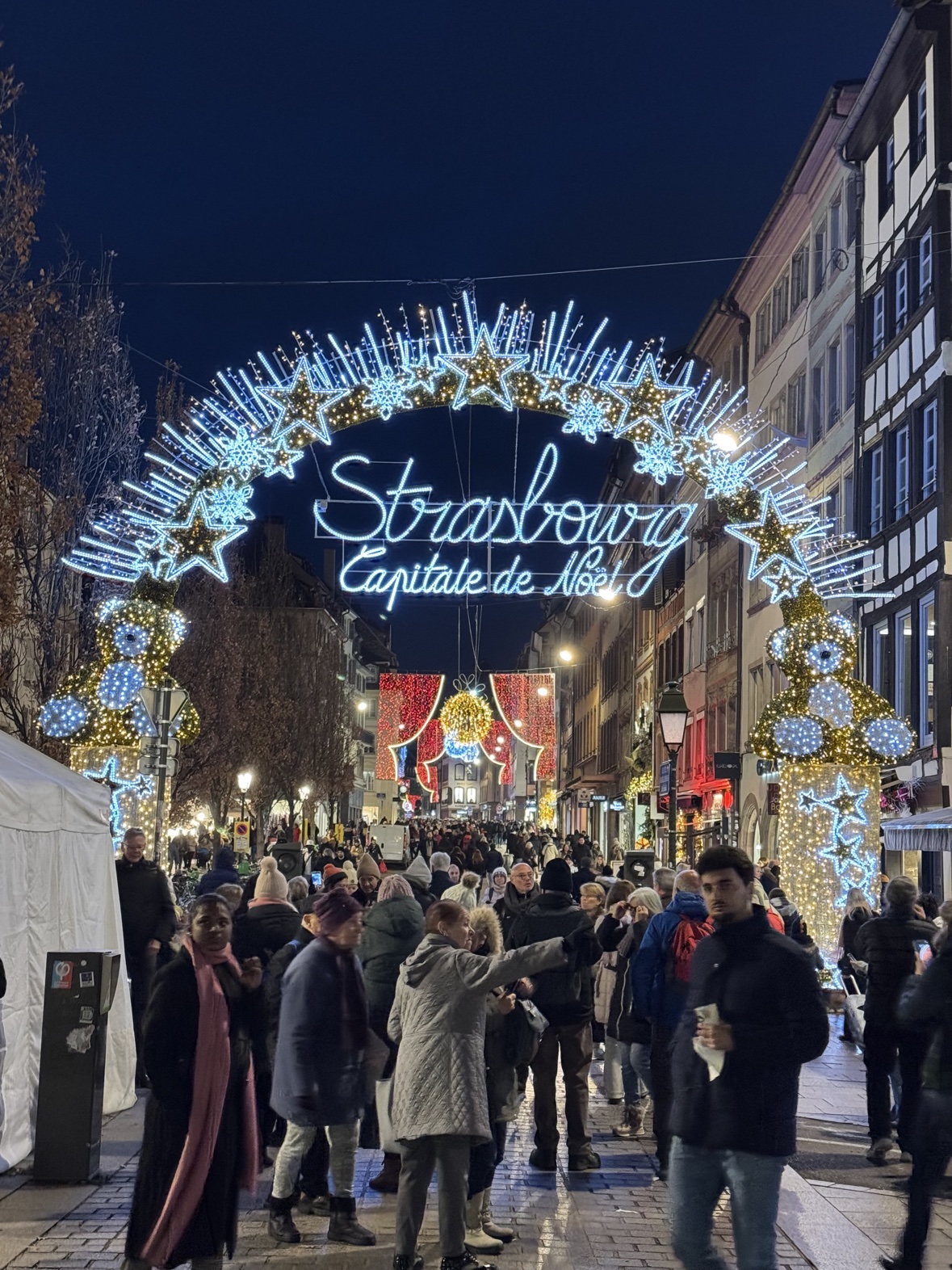 Strasbourg's illuminated Capitale de Noël arch over a crowded market street at night