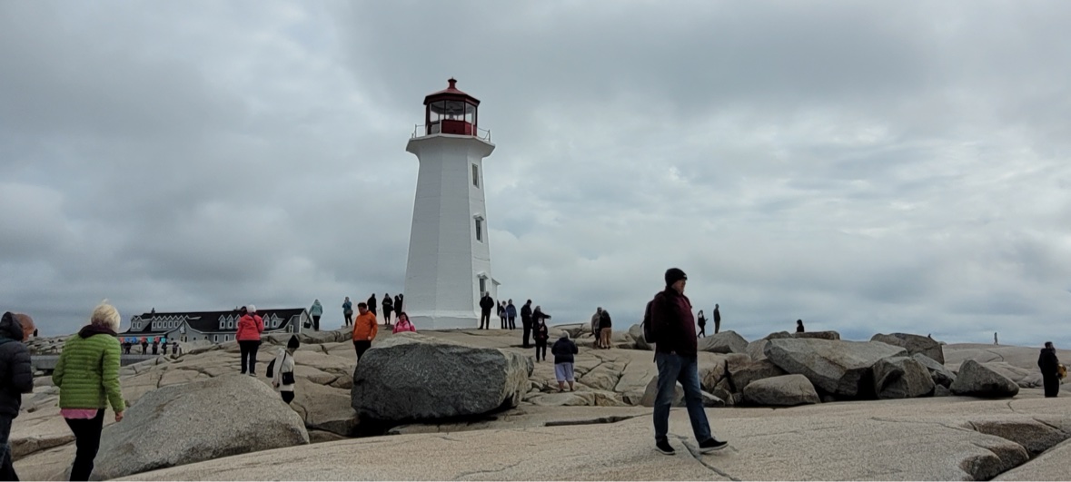 Peggy's Cove lighthouse on the granite rocks under a cloudy sky, with visitors exploring, Nova Scotia