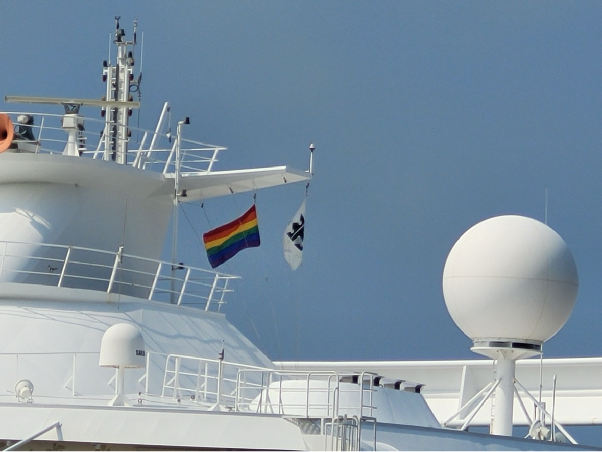 A rainbow Pride flag flying from the mast of a cruise ship